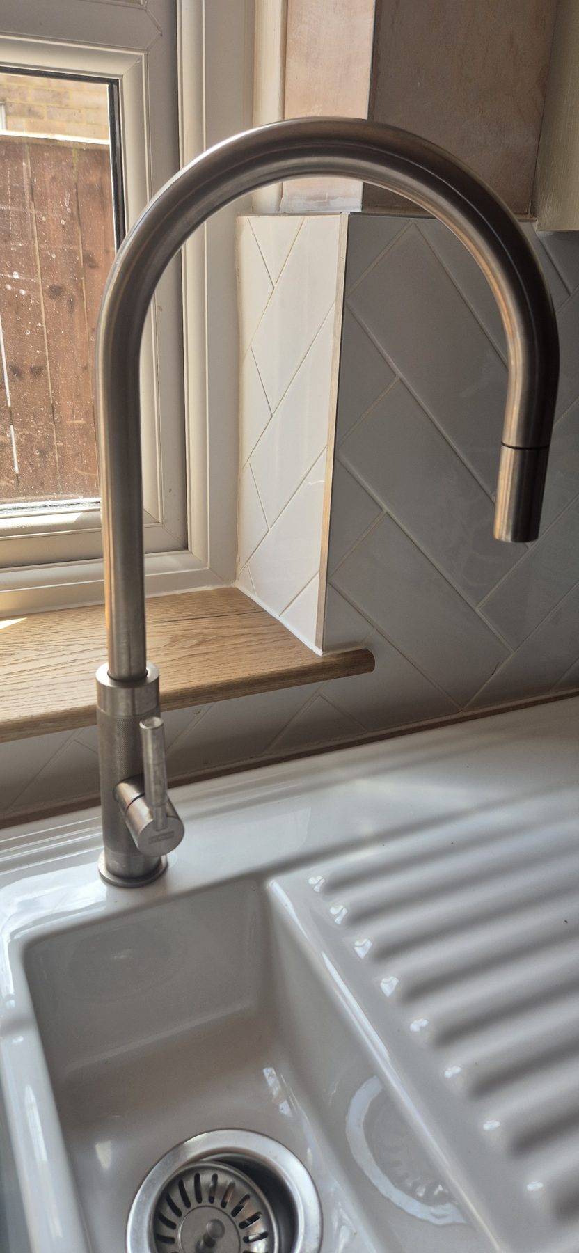 A brushed steel pull-out mixer tap over a white sink with a ribbed drainer