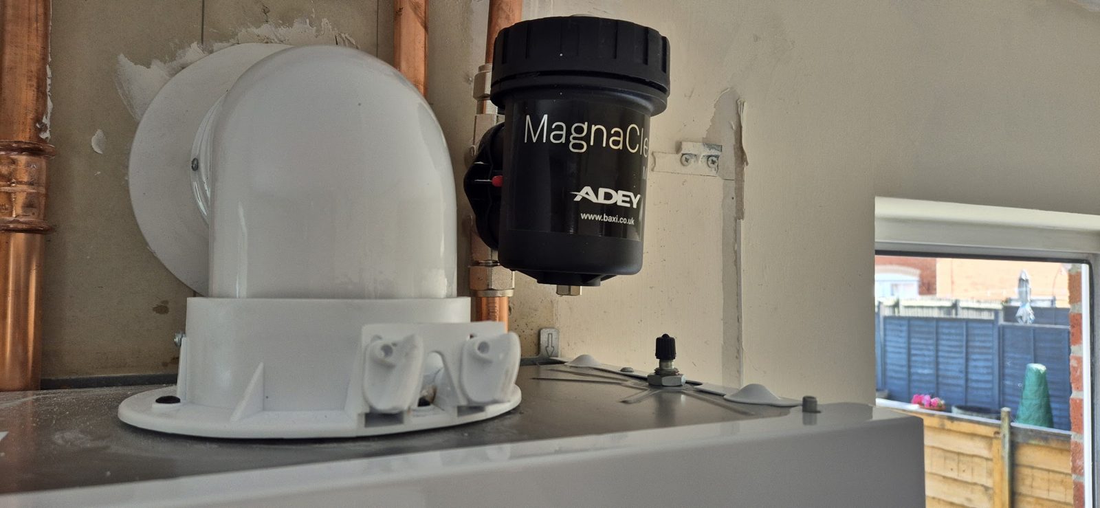 A white boiler flue elbow and a MagnaClean filter fitted on a new boiler with copper pipes