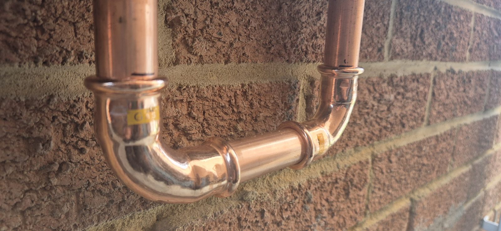 A neat copper press-fit pipe elbow fixed to a brick wall