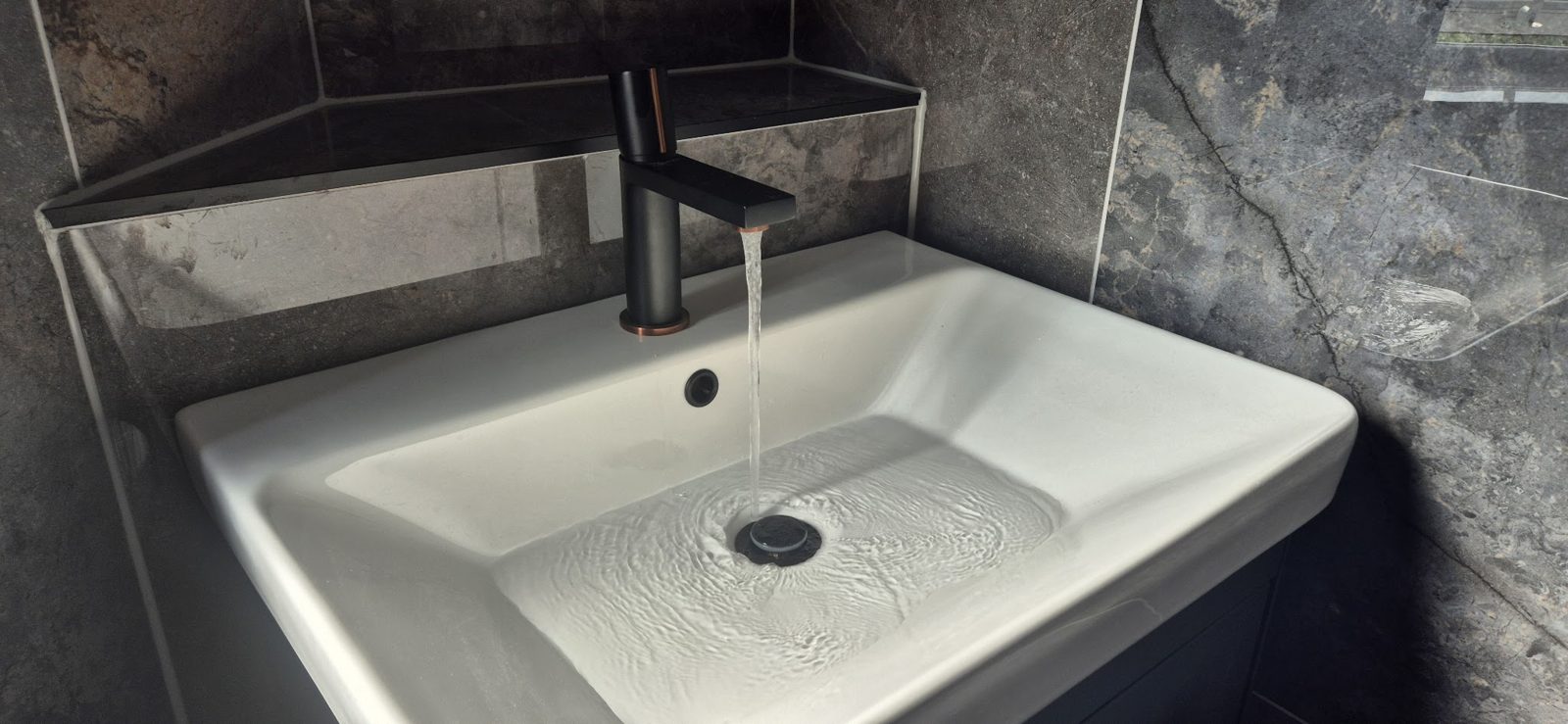 A basin with a running tap on dark stone effect tiles