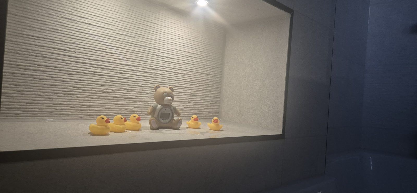 A tiled bath niche with yellow rubber ducks and a teddy bear